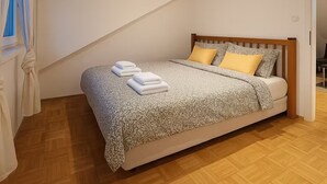 A bedroom with a wooden bed, a sloped ceiling, and a window with curtains. - KindStay Suite 2 bedroom Apartment w/ Free Parking near Prague Airport (Praha-Zapad)