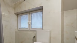 A bathroom with a toilet, a window with blinds, and a shower area. - KindStay Suite 2 bedroom Apartment w/ Free Parking near Prague Airport (Praha-Zapad)