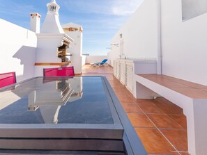 Eine Dachterrasse mit Glastisch, blauen Loungestühlen und einem weißen Gebäude mit Schornstein.