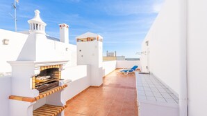 Una terrazza sul tetto con una griglia integrata, una poltrona da relax blu e una vista libera sul mare.