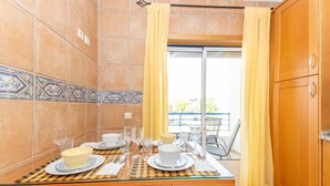 Zona pranzo con tavolo imbandito per quattro persone, una porta vetrata scorrevole che dà su un balcone e un mobiletto in legno sulla destra.