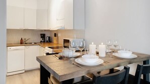 Une cuisine moderne avec des meubles blancs, une table à manger en bois pour quatre personnes et une machine à café.
