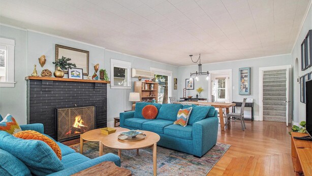 A living room with a fireplace, blue sofa, wooden coffee table, and a dining area with a table and chairs.