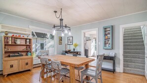 A dining area with a wooden table and chairs, a chandelier, and a bookshelf with various items.