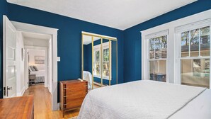 A bedroom with a large bed, a dresser, a mirror, and a door leading to another room.