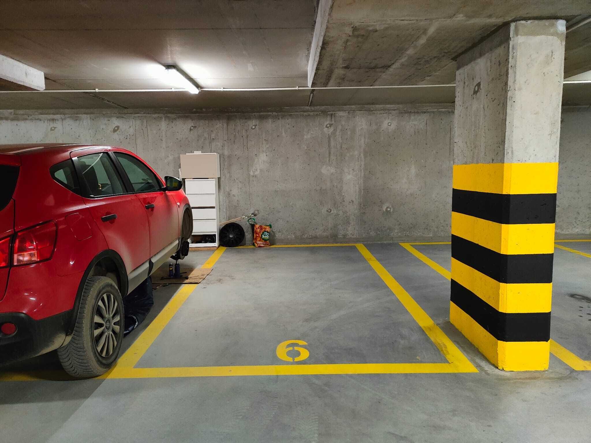 Un parcheggio sotterraneo con un'auto rossa parcheggiata in uno stallo contrassegnato col numero 6.