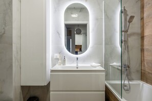 Ein modernes Badezimmer mit Marmor-Waschtisch, einer Glastrennwand-Dusche und einem runden Spiegel.