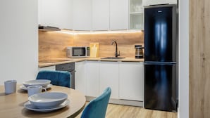 A modern kitchen with white cabinets, a black refrigerator, a microwave, and a coffee maker. - LILY APART the Big Screen Apartment (Gdańsk)