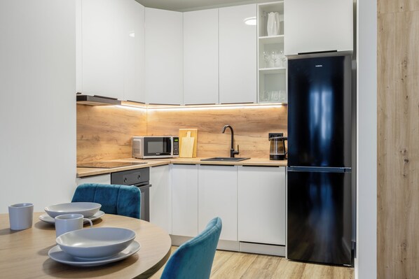 A modern kitchen with white cabinets, a black refrigerator, a microwave, and a coffee maker.