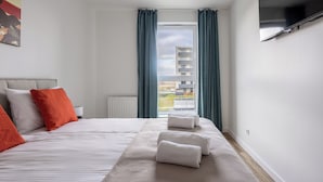 A modern hotel room with a large bed, a flat-screen TV, and a window with curtains. - LILY APART the Big Screen Apartment (Gdańsk)