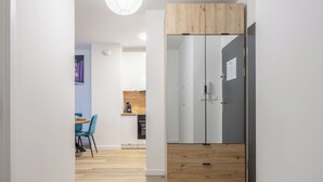 A modern kitchen with a wooden cabinet, a refrigerator, and a dining area with chairs and a table. - LILY APART the Big Screen Apartment (Gdańsk)
