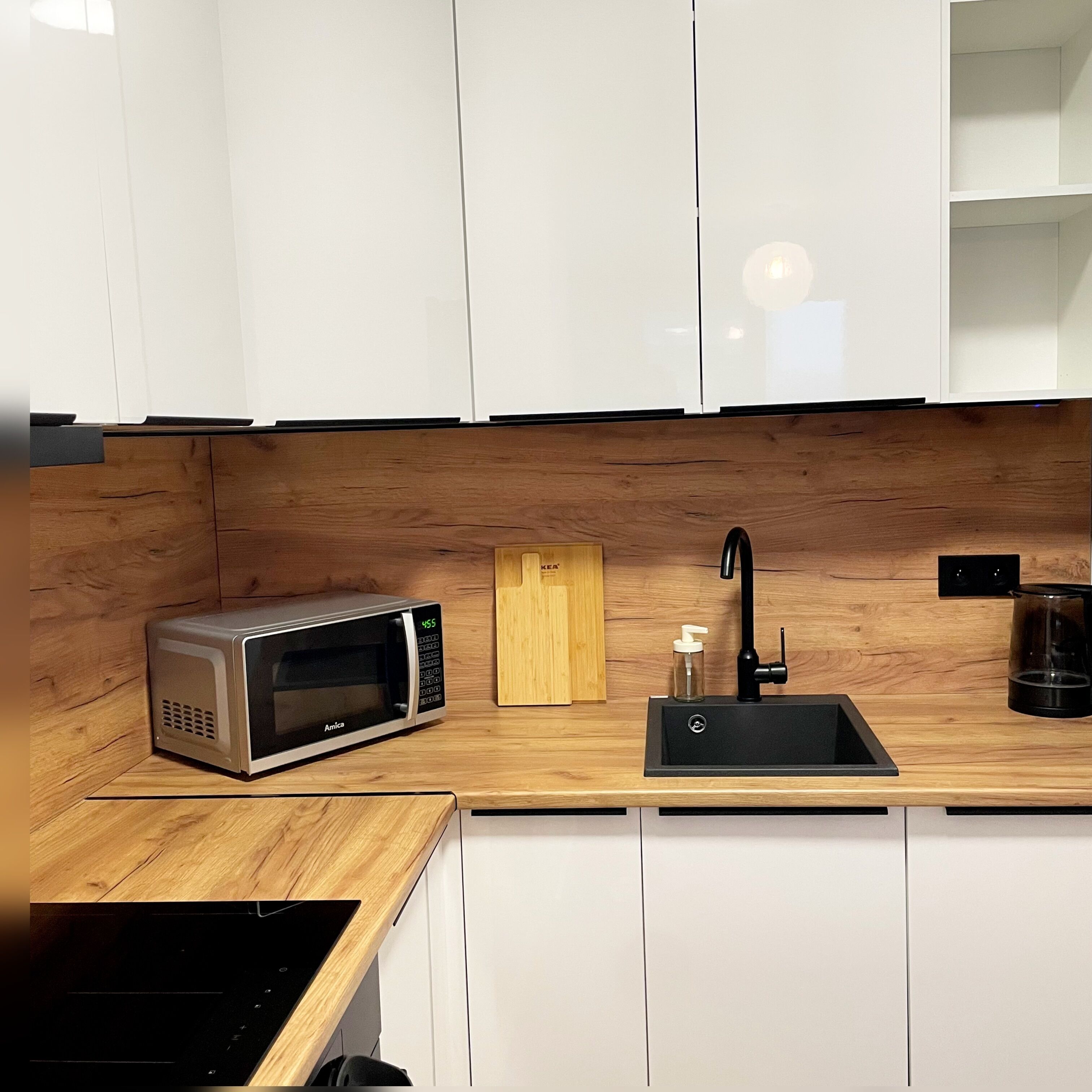 A modern kitchen with white cabinets, a wooden countertop, a microwave, a sink, and a coffee maker.