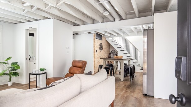 A spacious living area with a sofa, a dining table, and a staircase leading to an upper level. - Two Beach Homes with 2 Hot Tubs Sleeps 20+ (Michigan City)