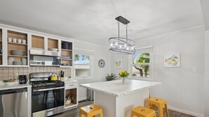 A modern kitchen with white cabinetry, stainless steel appliances, and a central island with stools. - Two Beach Homes with 2 Hot Tubs Sleeps 20+ (Michigan City)