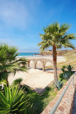 A coastal view with a palm tree, a stone bridge, and a beach. - Rosarito Jr Penthouse at La Jolla Excellence (Playas de Rosarito)