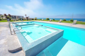 Piscina com borda em azulejo, espreguiçadeiras e vista para o oceano.
