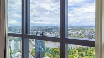 A room with large windows offering a cityscape view, including buildings and greenery.