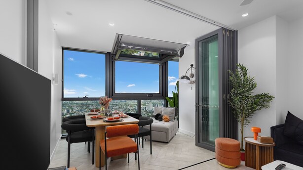 Ein moderner Wohnraum mit Essbereich, Sitzgelegenheiten, einer Couch, einem Couchtisch und einem großen Fenster mit Blick auf die Stadt.