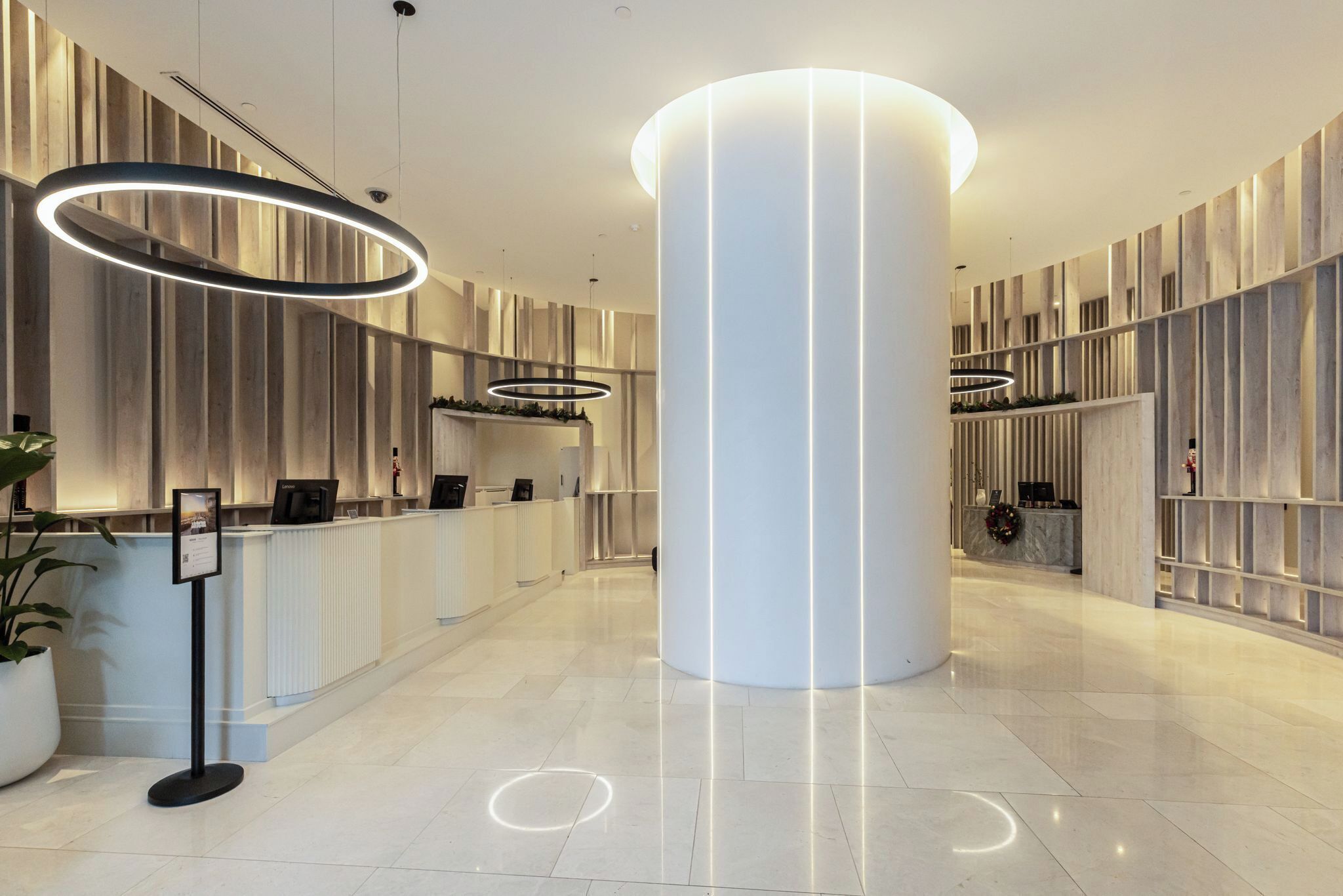 A modern hotel lobby with a reception desk, a large central pillar, and contemporary lighting fixtures.
