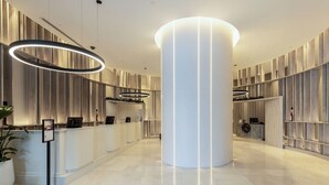 Eine moderne Hotellobby mit einer Rezeption, einer großen zentralen Säule und zeitgemäßer Beleuchtung.