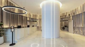 A modern hotel lobby with a reception desk, a large central pillar, and contemporary lighting fixtures.