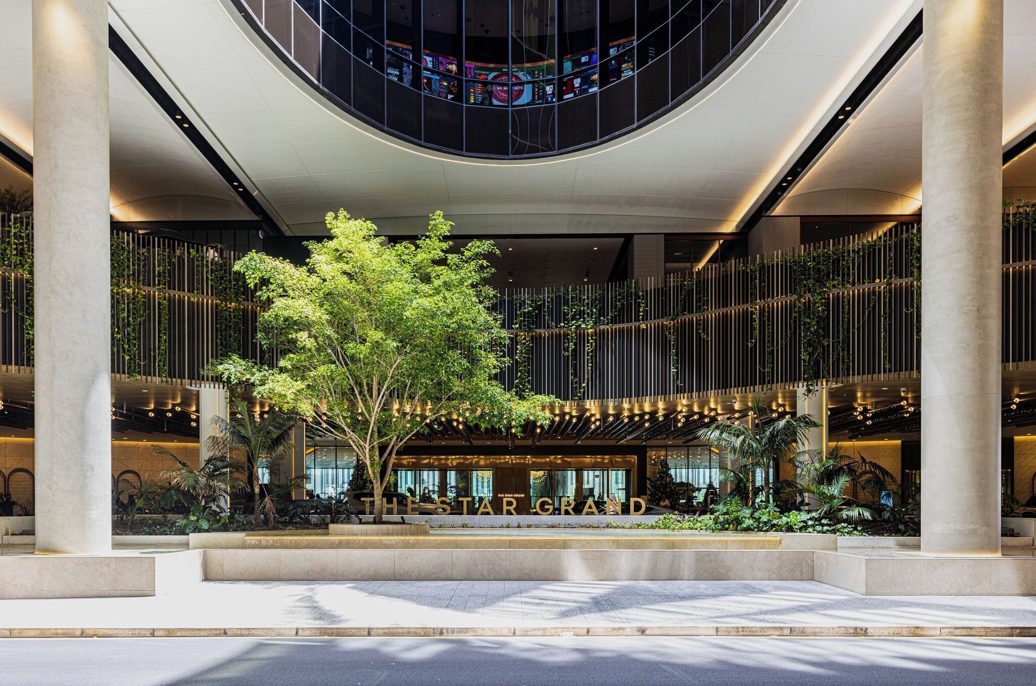 Ingresso moderno di un hotel con un grande albero, colonne e un cartello con scritto 'The Star Grand'.