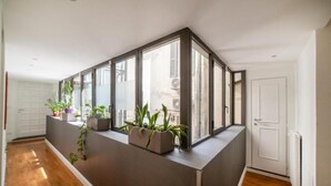 Um interior moderno com um banco embutido ao longo de uma parede de vidro, plantas em vasos e piso de madeira.