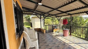 A covered outdoor area with a tiled floor, plastic chairs, a trash bin, and a red cloth hanging on a railing. - PARCEROS GROUP - 4-BEDROOM VACATION FARM, MORELIA, PEREIRA, COLOMBIA (La Estrella)
