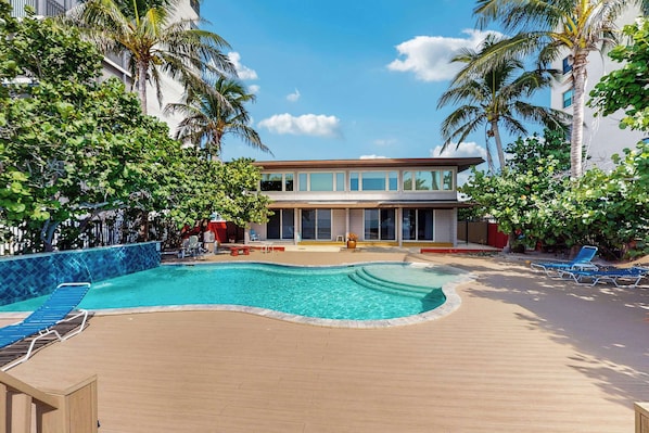 A pool area with a modern building, palm trees, and lounge chairs.