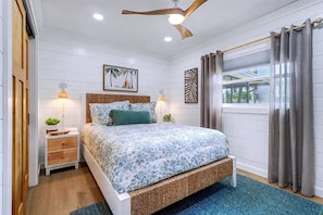 A bedroom with a bed, bedside tables, a ceiling fan, a window with curtains, and a view of the outdoors. - Island getaway steps from the beach with pool (Indian Rocks Beach)