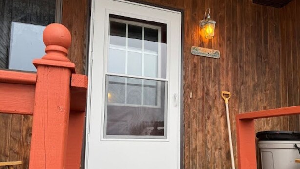 Fachada de madera con una puerta blanca, un farol y una escoba apoyada en la pared.