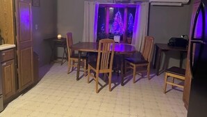 Un comedor con una mesa redonda y sillas, una araña y vista a un árbol de Navidad a través de una ventana.