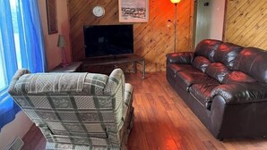 Una sala de estar acogedora con suelo de parqué de espiga, un sofá de cuero, un sillón a cuadros, un televisor de pantalla plana y una lámpara.