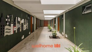 Un corridoio ben illuminato con un cartello 'welhome', piante in vaso e un murale con una veduta sulla città.