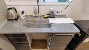 Una cucina compatta con lavandino in acciaio inossidabile, bollitore, ventilatore ed erogatore di sapone.