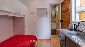 Una habitación pequeña con cama, kitchenette y baño reducido.