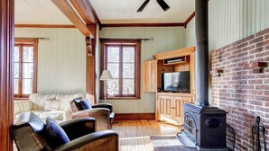A cozy living room with a fireplace, wooden furniture, and a television. - The Historic Post Office, Le Bureau de Poste (Lac-des-Plages)