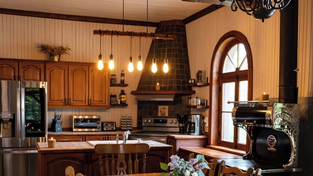 A spacious kitchen with wooden cabinets, a large island, and a built-in grill. - The Historic Post Office, Le Bureau de Poste (Lac-des-Plages)