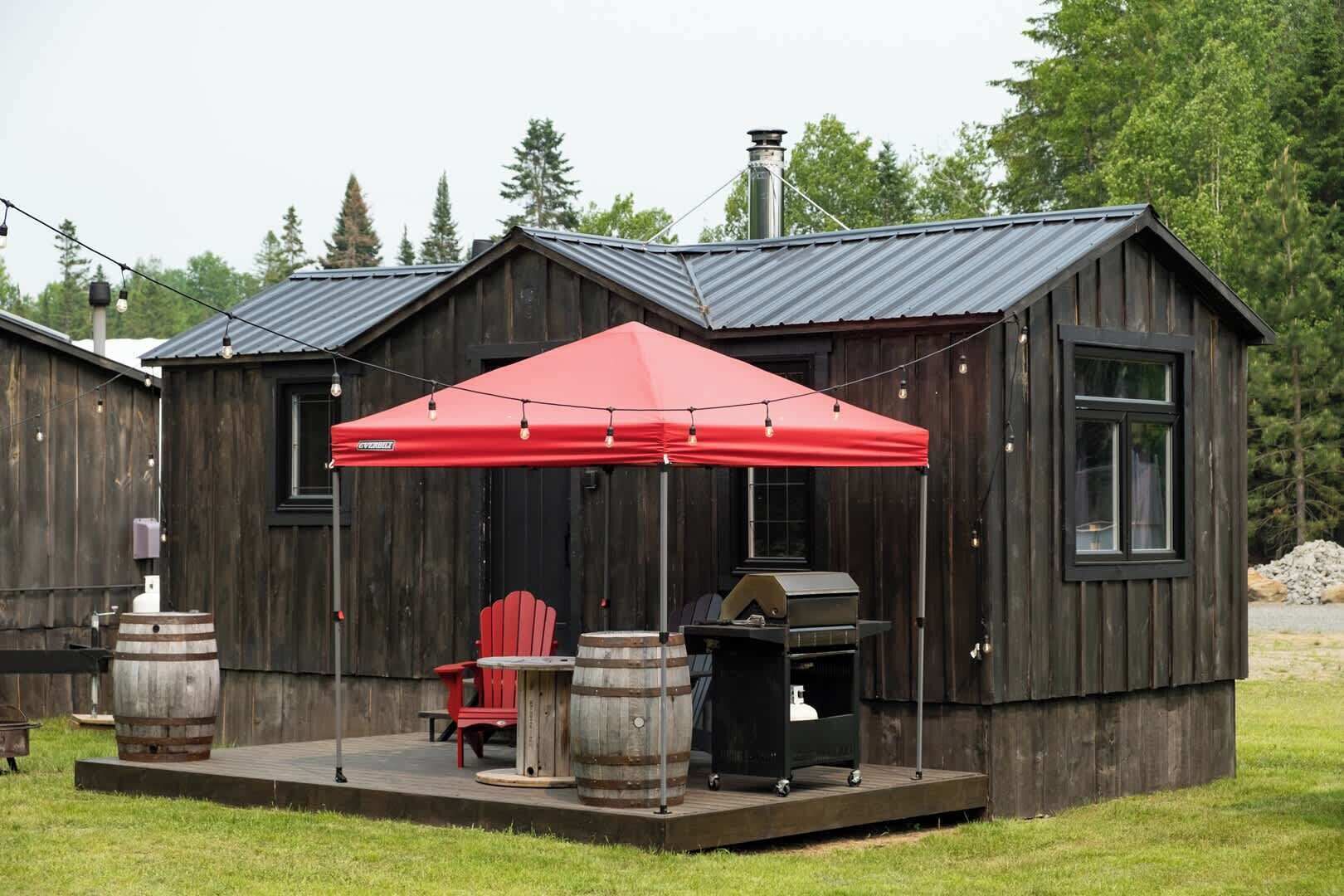Un rustico chalet di legno con un tetto sporgente rosso, una griglia e una sedia rossa.