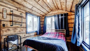 Een gezellig chaletkamer met houten plafond, een bed met een geruit plaid, een verwarming en een raam met gordijnen.