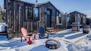 Een houten hut met terras, zitplaatsen buiten en een barbecuehoek.