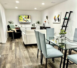 Un comedor moderno con una mesa y sillas de vidrio, un televisor montado en la pared y plantas decorativas.