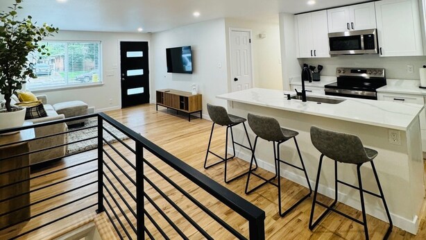 A modern kitchen with white cabinets, a black countertop, and a stainless steel microwave. There are three bar stools and a wooden dining table. - A Sleek Modern 4-bedroom house with updated amenities in welcoming Westminster (Westminster)