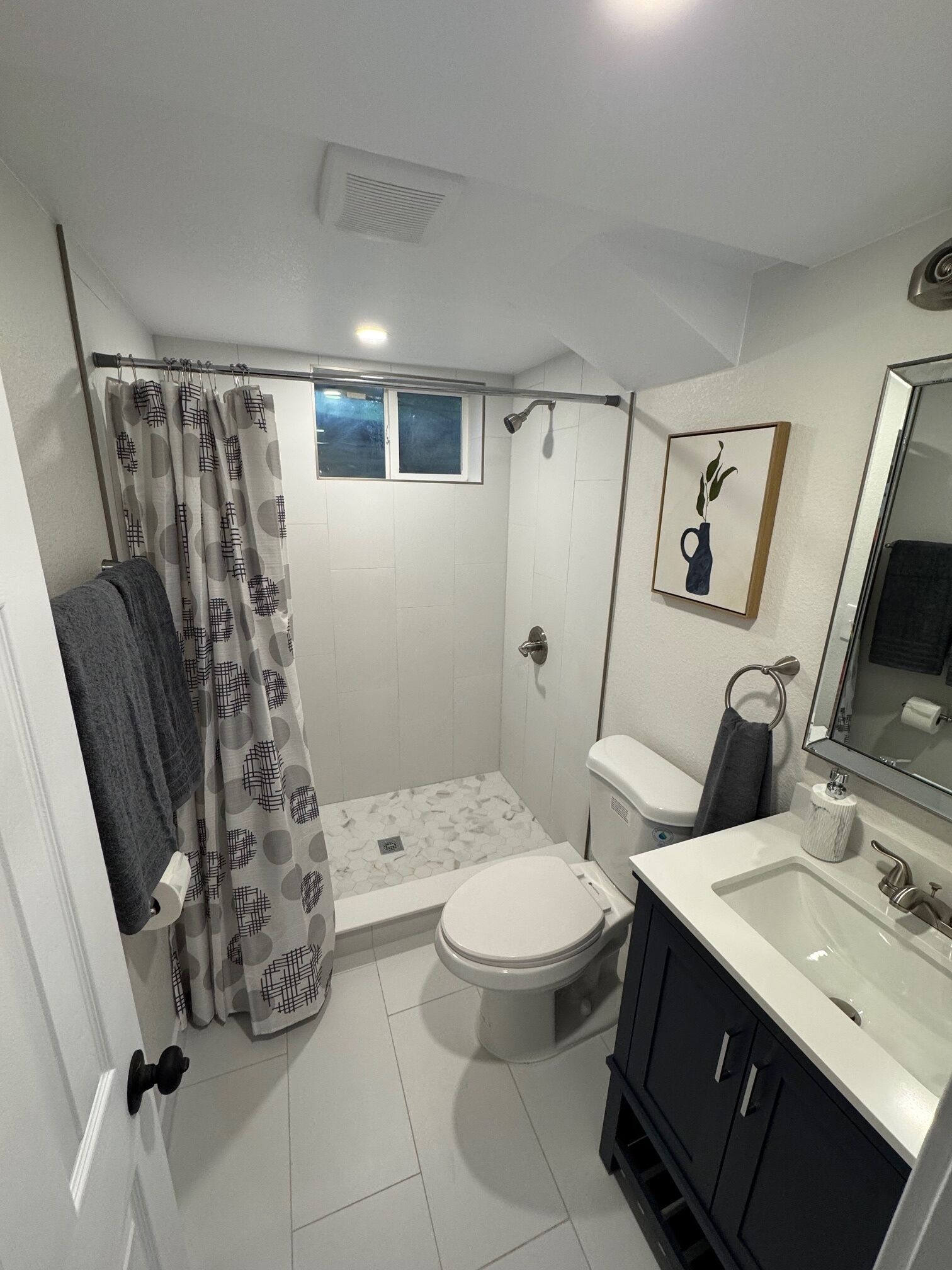 A bathroom with a shower, toilet, sink, and a mirror.