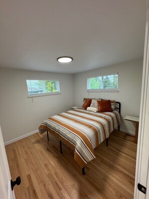 Ein Schlafzimmer mit einem Bett, zwei Fenstern, einem Nachttisch und einer Tür.