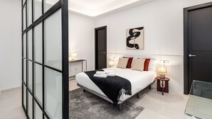 A modern bedroom with a large bed, two bedside tables, a wall-mounted abstract art piece, and a glass partition. - Waou Urban Home Salamanca V (Madrid)