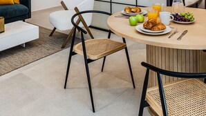 A modern living room with a dining area, featuring a large glass partition, a sofa, a chair, and a table set with breakfast. - Waou Urban Home Salamanca V (Madrid)