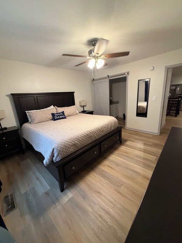 A bedroom with a bed, nightstands, a ceiling fan, a mirror, and a door leading to a bathroom. - Fantastic 2-bedroom 2 Bath townhome in charming Forest City. Built in 2023 (Forest City)
