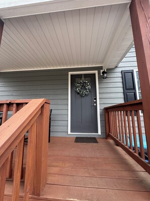 A wooden front porch with a dark gray door, a wooden railing, and a wreath on the door. - Fantastic 2-bedroom 2 Bath townhome in charming Forest City. Built in 2023 (Forest City)