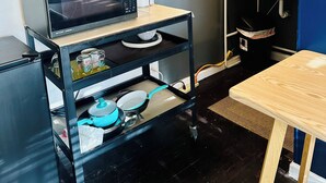 Una cocina compacta con un microondas sobre un carrito, una tetera y varios recipientes.